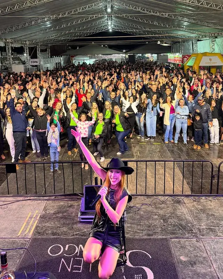 Rafaela Martins de chapéu no palco, com a tenda lotada atrás